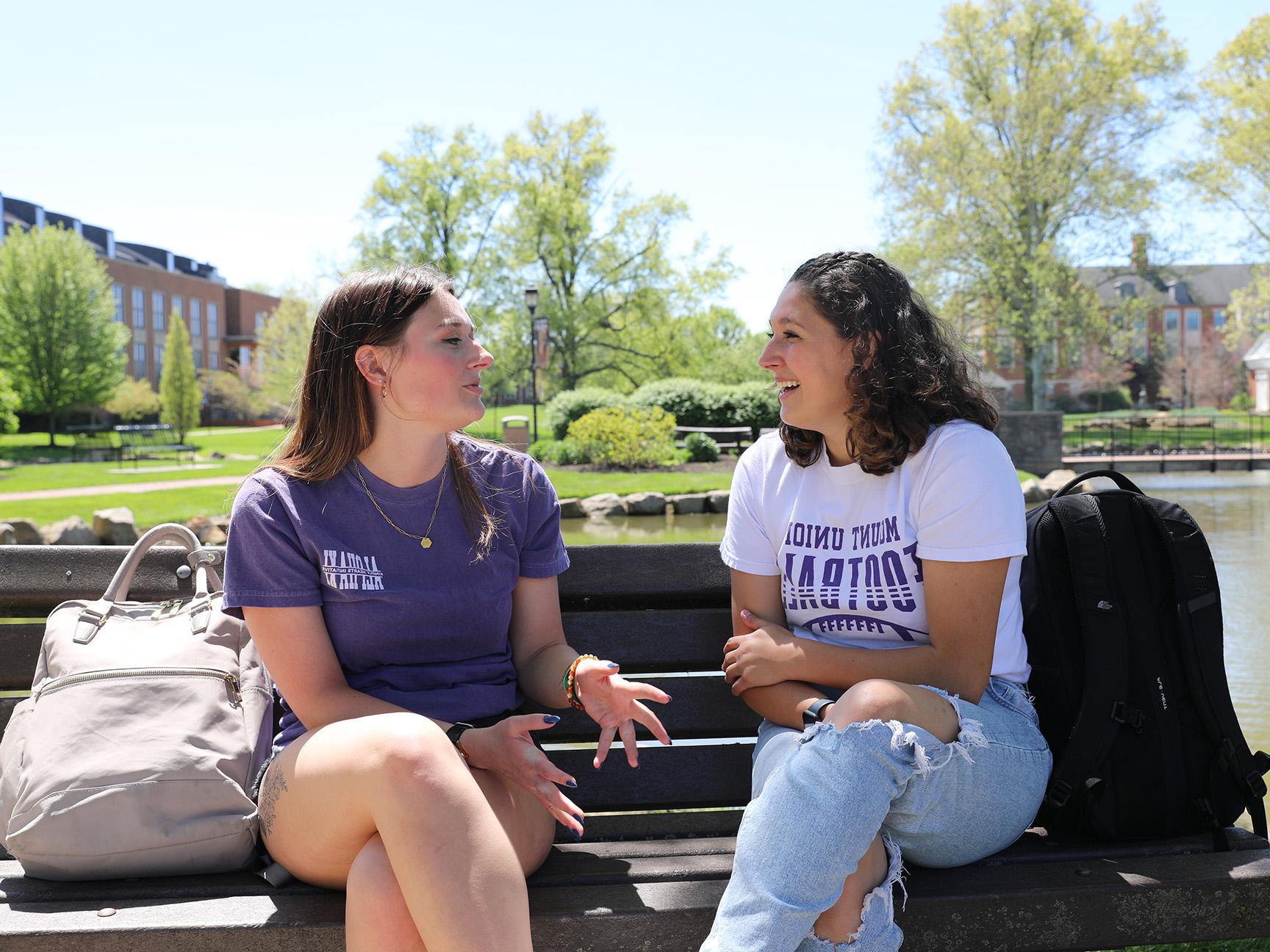 Two students sitting on a bench alongside the Campus Lakes