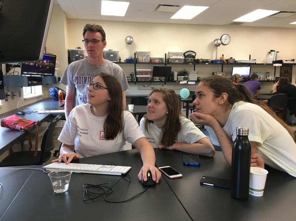 three students looking at computer while professor looks on